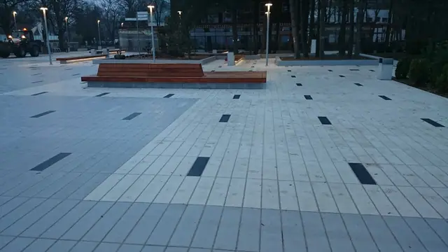 Wieczorny widok ukończonego placu przy molo w Kołobrzegu z drewnianą ławką i ciemnymi wstawkami w płytach