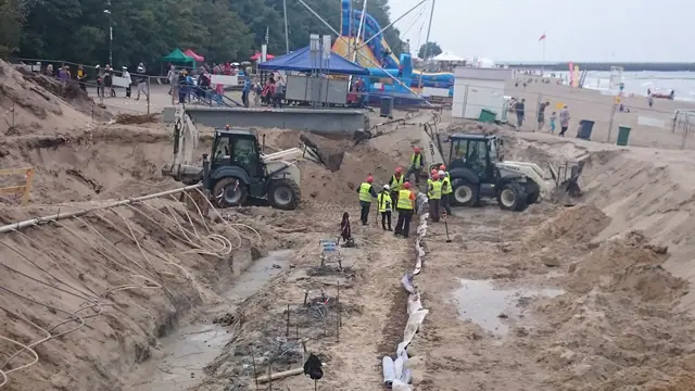 Koparka kopie wykop liniowy wzdłuż wydmy obok plażowych atrakcji podczas prac przy molo w Kołobrzegu