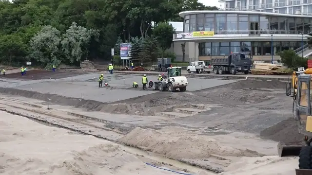 Robotnicy i koparka wyrównują podłoże przed betonowaniem placu w sąsiedztwie hotelu przy molo w Kołobrzegu