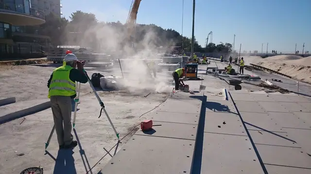 Robotnicy zacierają świeżo wylany beton nawierzchni w obłoku pyłu przy molo w Kołobrzegu