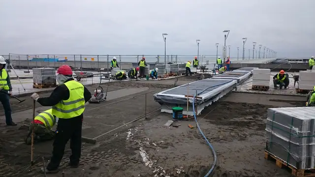 Robotnik rozprowadza zaprawę pod wielkoformatową płytę prefabrykowaną przygotowaną do montażu przy molo w Kołobrzegu