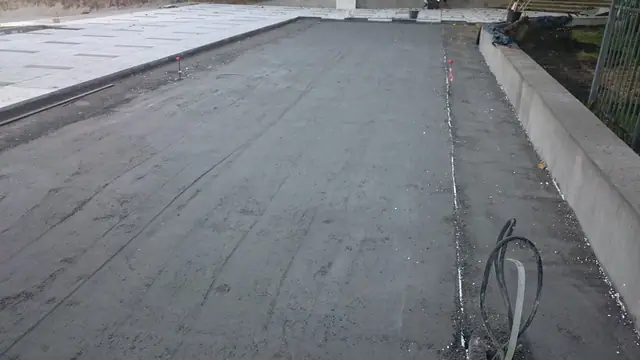 Świeżo zatarta powierzchnia betonowa placu z widocznymi dylatacjami obok muru oporowego przy molo w Kołobrzegu