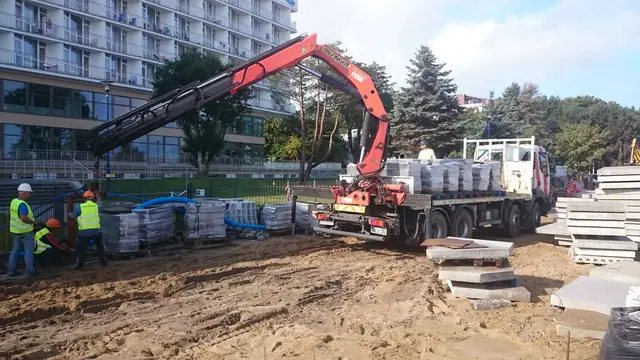 Żuraw samochodowy rozładowuje płyty granitowe z naczepy dla robotników na placu budowy przy molo w Kołobrzegu