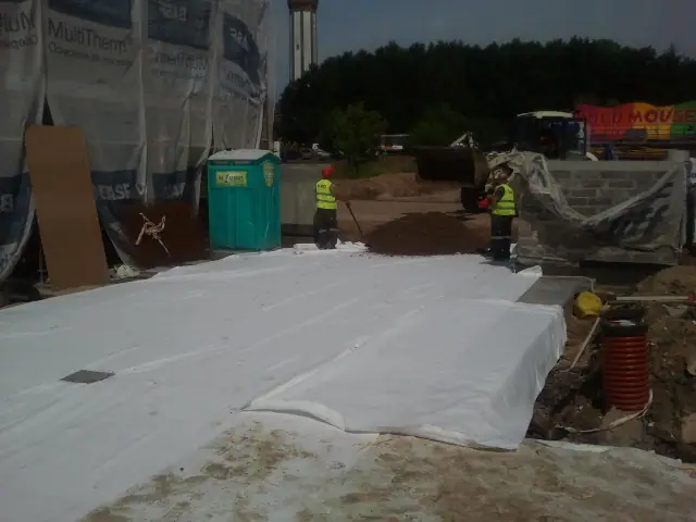 Biała membrana hydroizolacyjna rozłożona pod nawierzchnię przy ocieplanej ścianie budynku