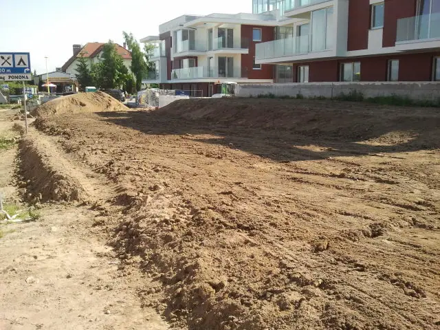 Długi pas wyrównanej ziemi wzdłuż krawężnika przygotowany pod nasadzenia przy hotelu
