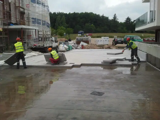 Robotnicy w kamizelkach odblaskowych układają duże płyty betonowe na tarasie przy hotelu Baltic Cliff