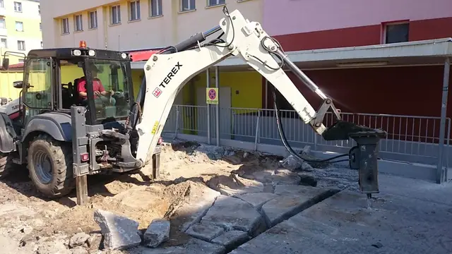 Koparko-ładowarka z młotem hydraulicznym rozkuwa starą nawierzchnię betonową