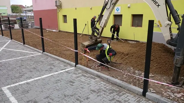 Koparka wykonuje wykop wzdłuż budynku pod podbudowę nowej drogi wewnętrznej