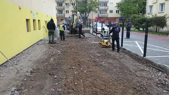 Pracownik zagęszcza podbudowę płytą wibracyjną wzdłuż wykopu przy drodze