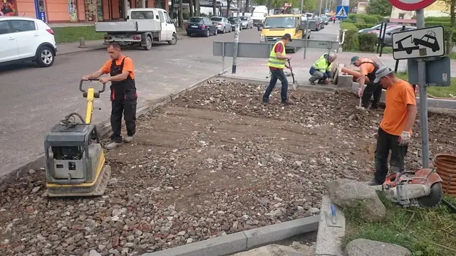 Dwóch pracowników zagęszcza podbudowę na wysepce przy ruchliwej ulicy