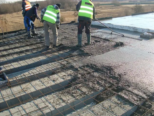 Robotnicy w kamizelkach odblaskowych betonują i zacierają zbrojony strop budynku mieszkalnego
