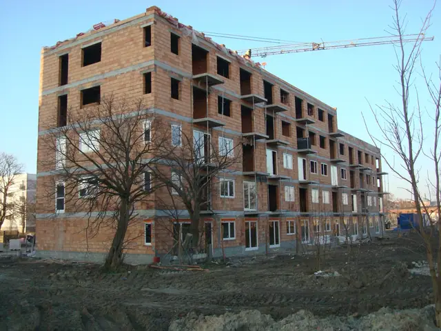 Budynek z czerwonej cegły bez tynku, w tle żuraw wieżowy i bezlistne drzewa