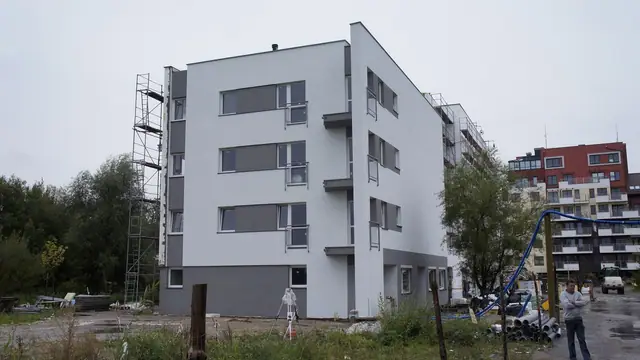 Budynek z jasną elewacją i pojedynczą drabiną przystawioną do ściany, obok zaparkowany samochód
