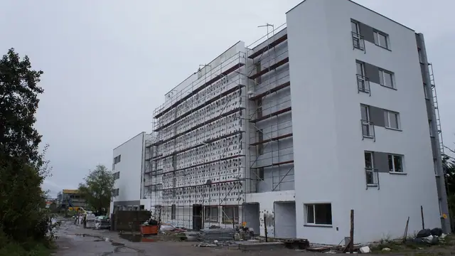 Otynkowany na biało budynek z rusztowaniami na elewacji przygotowanymi do ocieplenia