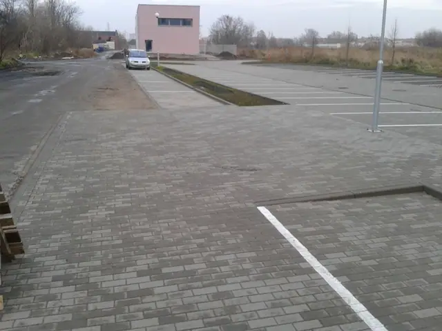 Nowy parking z kostki brukowej przy budynku, w tle różowy budynek gospodarczy
