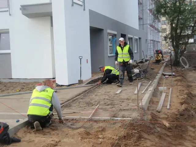 Robotnicy układają kostkę brukową i krawężniki przy elewacji gotowego budynku mieszkalnego