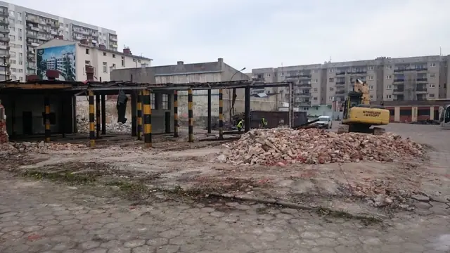 Koparka pracuje wśród ceglanego gruzu podczas trwających prac rozbiórkowych bazy PKS