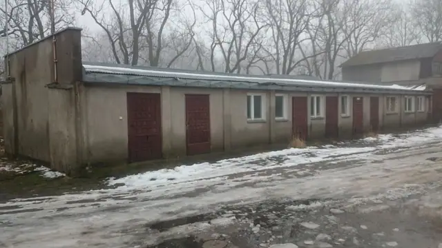 Długi rząd starych garaży z czerwonymi bramami blaszanymi przed rozbiórką na terenie bazy