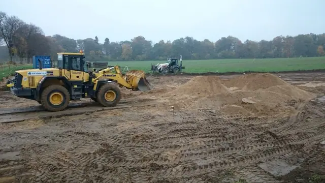 Ładowarka wyrównuje piaszczysty plac składowy, widoczne ślady kół maszyn