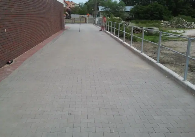 Chodnik z kostki brukowej z poręczą wzdłuż ceglanego muru przy placu budowy