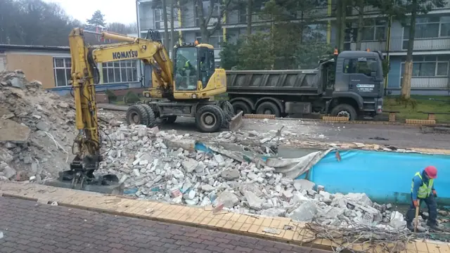 Koparka kołowa z łyżką pracuje przy gruzie obok basenu i samochodu ciężarowego w Centrum Verano
