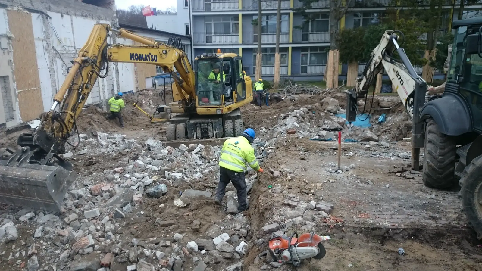 Koparki pracują przy hałdzie gruzu, robotnik w kamizelce nadzoruje prace przy Centrum Verano w Kołobrzegu