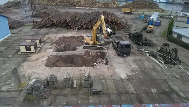 Koparka pracuje przy wykopie i stertach materiałów na terenie po rozbiórce