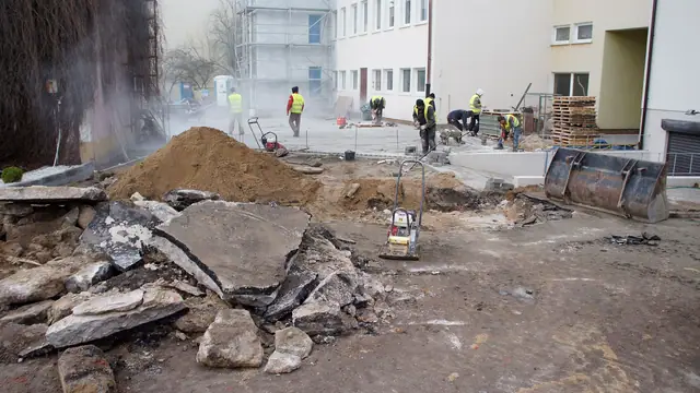 Robotnicy w kłębach kurzu demontują starą nawierzchnię betonową młotami pneumatycznymi
