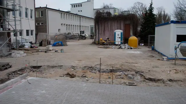 Plac częściowo wyłożony kostką brukową, w tle namiot i zaplecze budowy