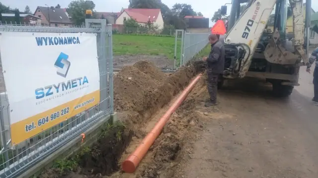 Baner wykonawcy Szymeta zawieszony na ogrodzeniu placu budowy w Skrzatuszu