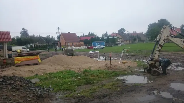 Koparko-ładowarka pracuje przy pryzmach piasku na rozmokłym terenie inwestycji w Skrzatuszu