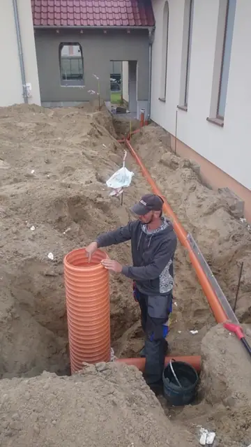 Robotnik łączy pomarańczowe rury kanalizacji deszczowej w wykopie tuż przy fundamencie budynku