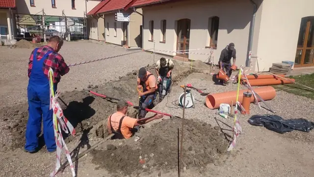 Ekipa montuje studzienkę kanalizacyjną z pomarańczowych rur tuż przy elewacji budynku