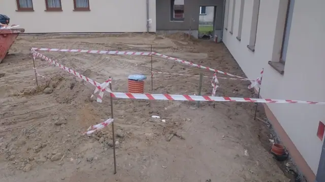 Taśmą ostrzegawczą odgrodzony fragment placu ze studzienką kanalizacyjną przy elewacji sanktuarium