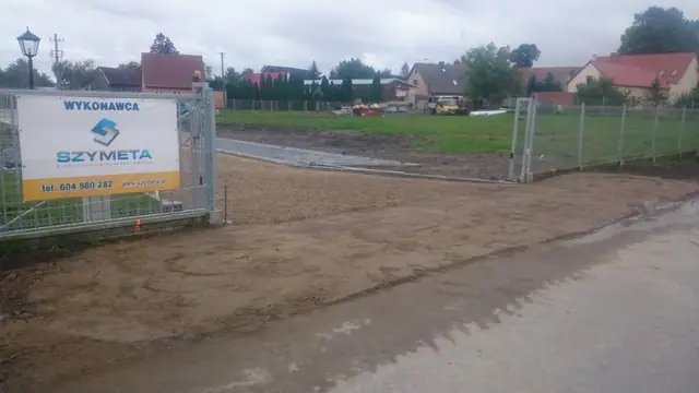 Gotowy plac z kostki brukowej ozdobiony donicami i ławkami, w tle wieża kościoła
