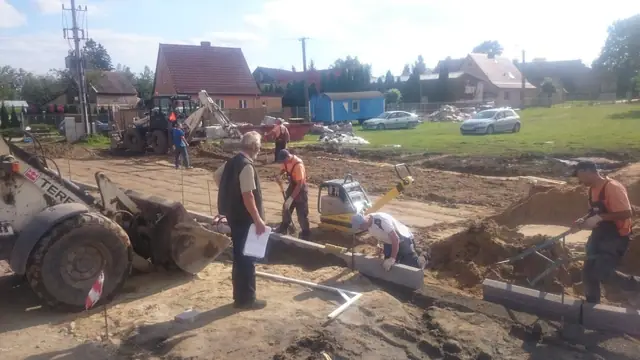 Zespół pracowników z koparką układa krawężniki wzdłuż wytyczonej trasy w Skrzatuszu