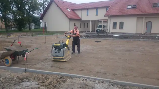 Ukończona nawierzchnia z ciemnej kostki brukowej przy ogrodzeniu z banerem Szymeta