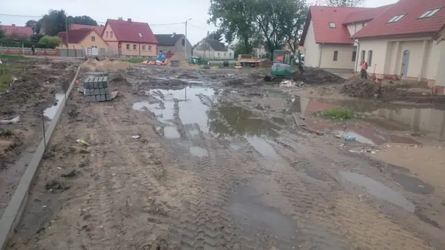 Ułożone krawężniki betonowe wzdłuż rozległego, rozmokłego placu przy zabudowaniach sanktuarium