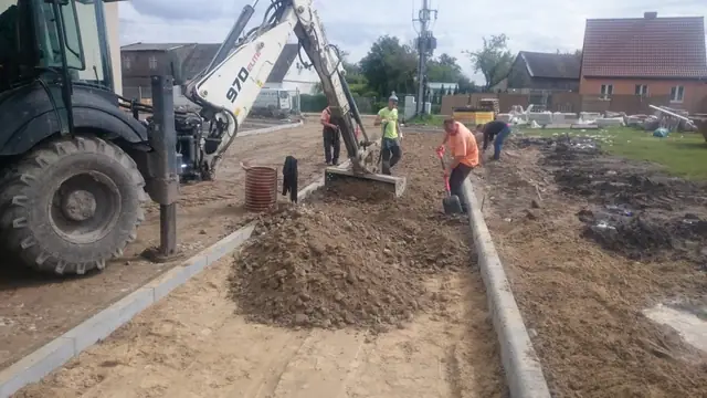 Ekipa w kamizelkach wykańcza krawędź korytka odwadniającego przy użyciu węża do polewania