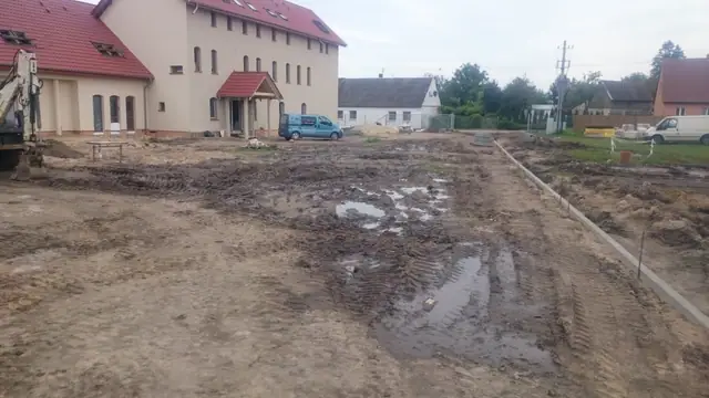Wyrównany plac przed budynkiem sanktuarium z widocznymi śladami kół i kałużami po deszczu