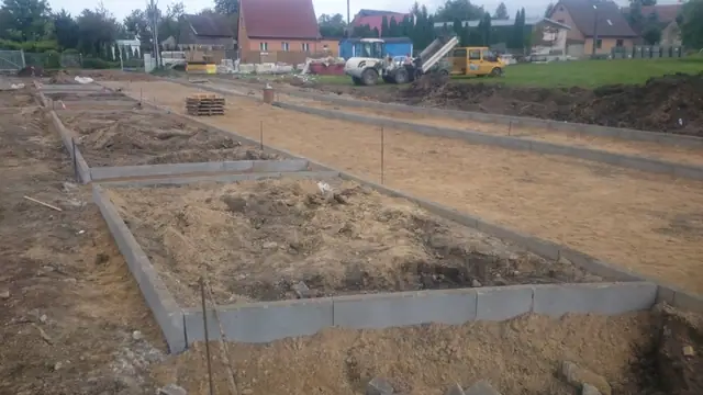 Pracownik zagęszcza podbudowę piaszczystą zagęszczarką płytową przy wózku budowlanym
