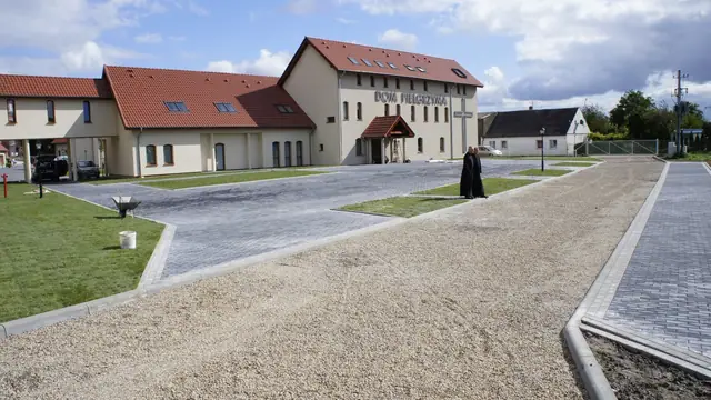 Wykończona żwirowa nawierzchnia alejki pomiędzy zadbanymi trawnikami przy zabudowaniach