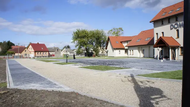 Żwirowa ścieżka prowadząca wzdłuż budynku Domu Pielgrzyma obok zaparkowanych samochodów