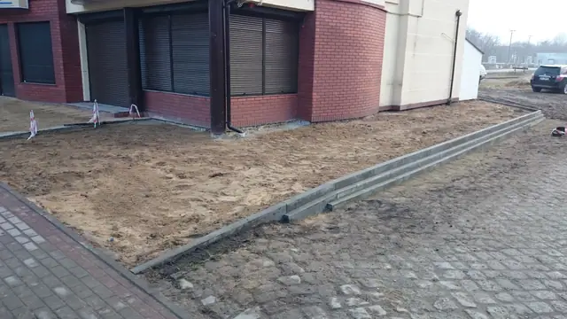 Gotowy kamienny krawężnik oddzielający piaszczystą rabatę od starej brukowanej drogi