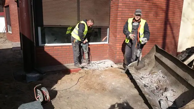 Dwaj robotnicy kruszą młotem starą nawierzchnię betonową przy wejściu do lokalu