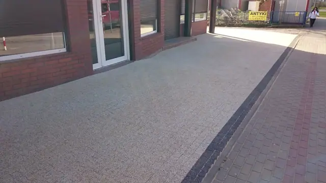 Nawierzchnia z płukanego betonu z ciemnym krawężnikiem i czerwonym akcentem z cegły przy wejściu