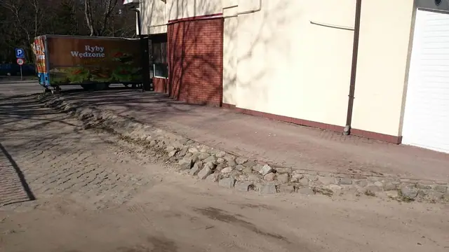 Zniszczony pas starego bruku obok budynku, przy którym zaparkowany jest samochód dostawczy