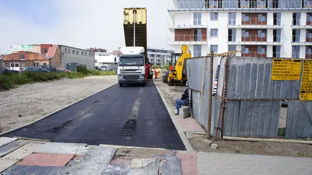 Ciężarówka i koparka przy świeżo ułożonym odcinku asfaltowej ścieżki obok bloków
