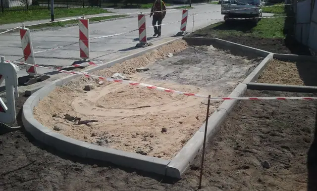 Zaokrąglony fragment betonowego krawężnika wokół piaszczystego kręgu ścieżki rowerowej