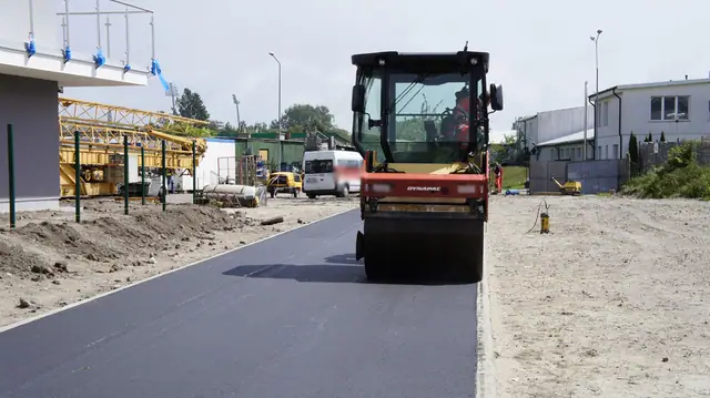 Świeżo ułożony czarny asfalt przy betonowym krawężniku i drewnianym szalunku